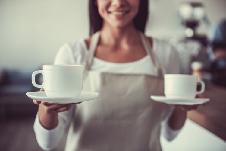 Portrait of a young girl happy barista that holds two cups of coffee for visitors in its cafe