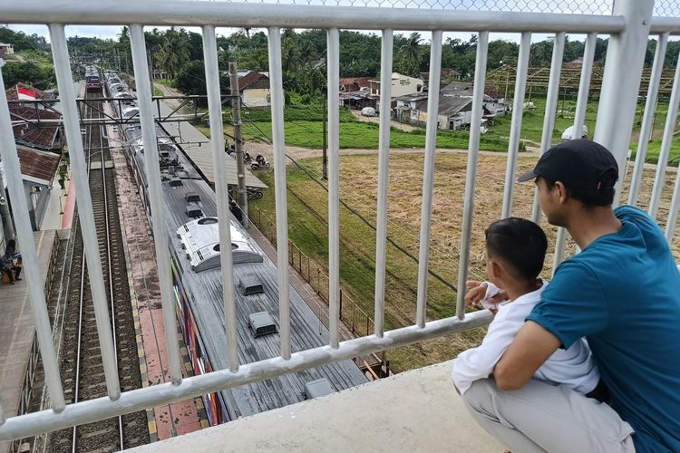 Damba Jaelani dan anaknya sedang asik melihat kereta dari atas JPO di Tenjo, Kabupaten Bogor, Kamis (23/10/2025).