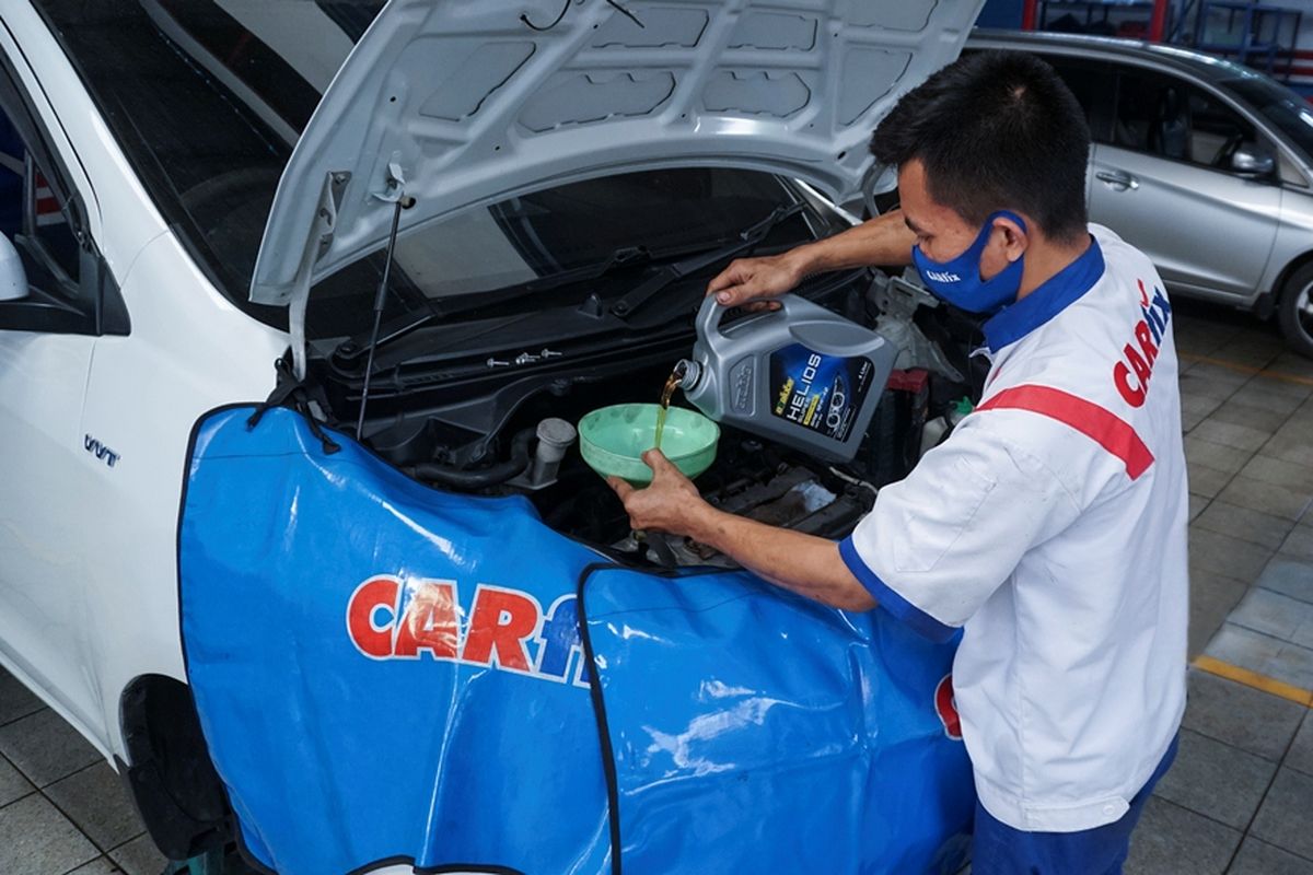 seorang mekanik tengah melakukan pengisian oli mesin mobil di bengkel carfix