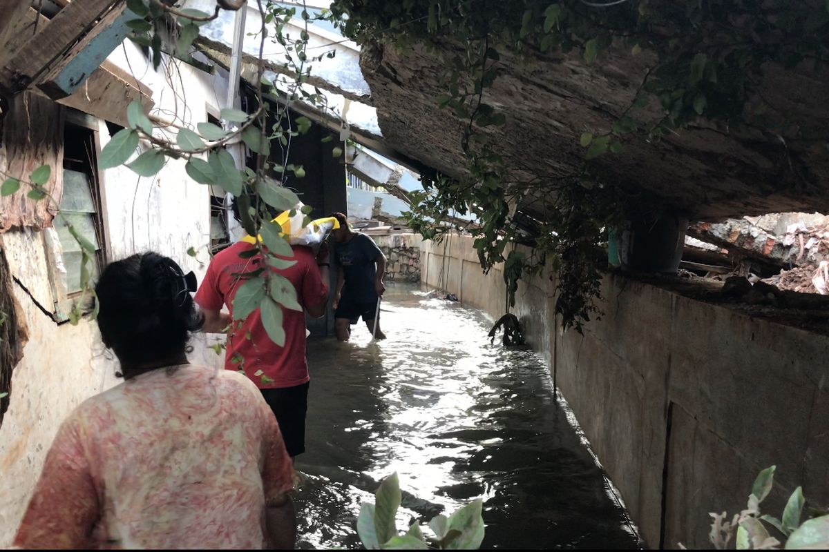 Warga berjalan di tengah banjir dan sela-sela reruntuhan tembok rumah milik warga Kavling Melati di Jalan Kemang Timur XI, Bangka, Mampang Prapatan, Jakarta Selatan pada Minggu (21/2/2021) sore. Reruntuhan tembok membuat saluran air tersumbat hingga menyebabkan banjir setinggi dua meter.