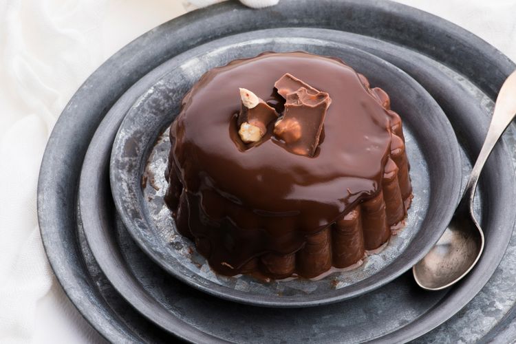 Ilustrasi puding cokelat dengan topping cokelat cair dan irisan cokelat batang. 