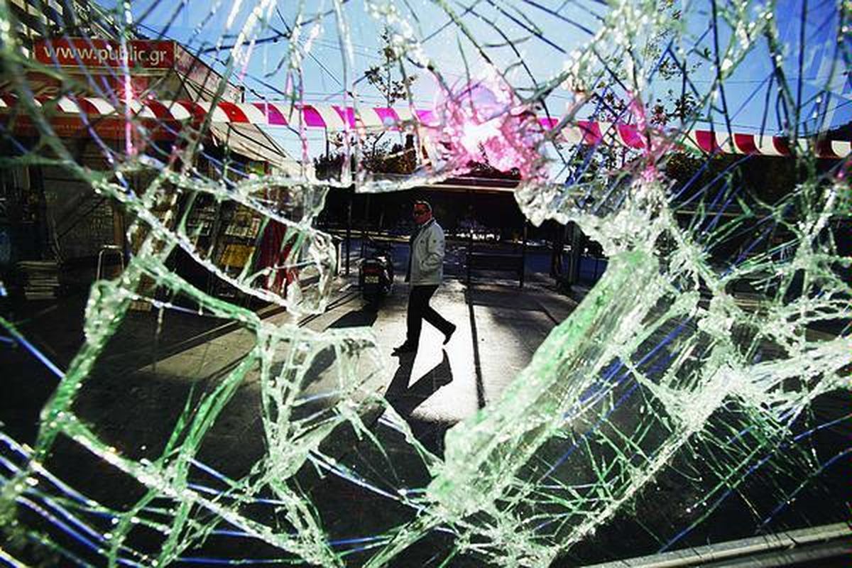 Seorang warga terlihat berjalan di balik kaca pecah di pertokoan Syntagma, Athena, Kamis (20/10). Aksi pengetatan ikat pinggang yang dilakukan Pemerintah Yunani memicu kemarahan publik. Hal itu mendorong mereka melancarkan tindak kekerasan.