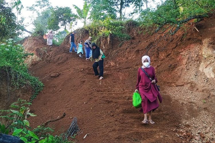 Sejumlah penyintas bencana yang akan mengikuti vaksinasi Covid-19 melintasi jalan setapak di atas longsoran Dusun Ciherang, Nyalindung, Sukabumi, Jawa Barat, Jumat (18/6/2021).