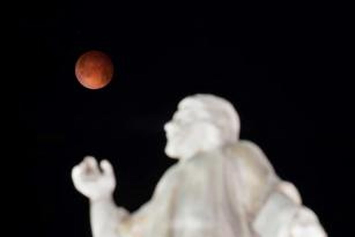 Gerhana bulan terlihat dengan latar depan Monumen El Salvador del Mundo di San Salvador, El Salvador, 15 April 2014. Gerhana bulan kali ini terbilang langka karena bulan berubah warna dari oranye ke merah darah.