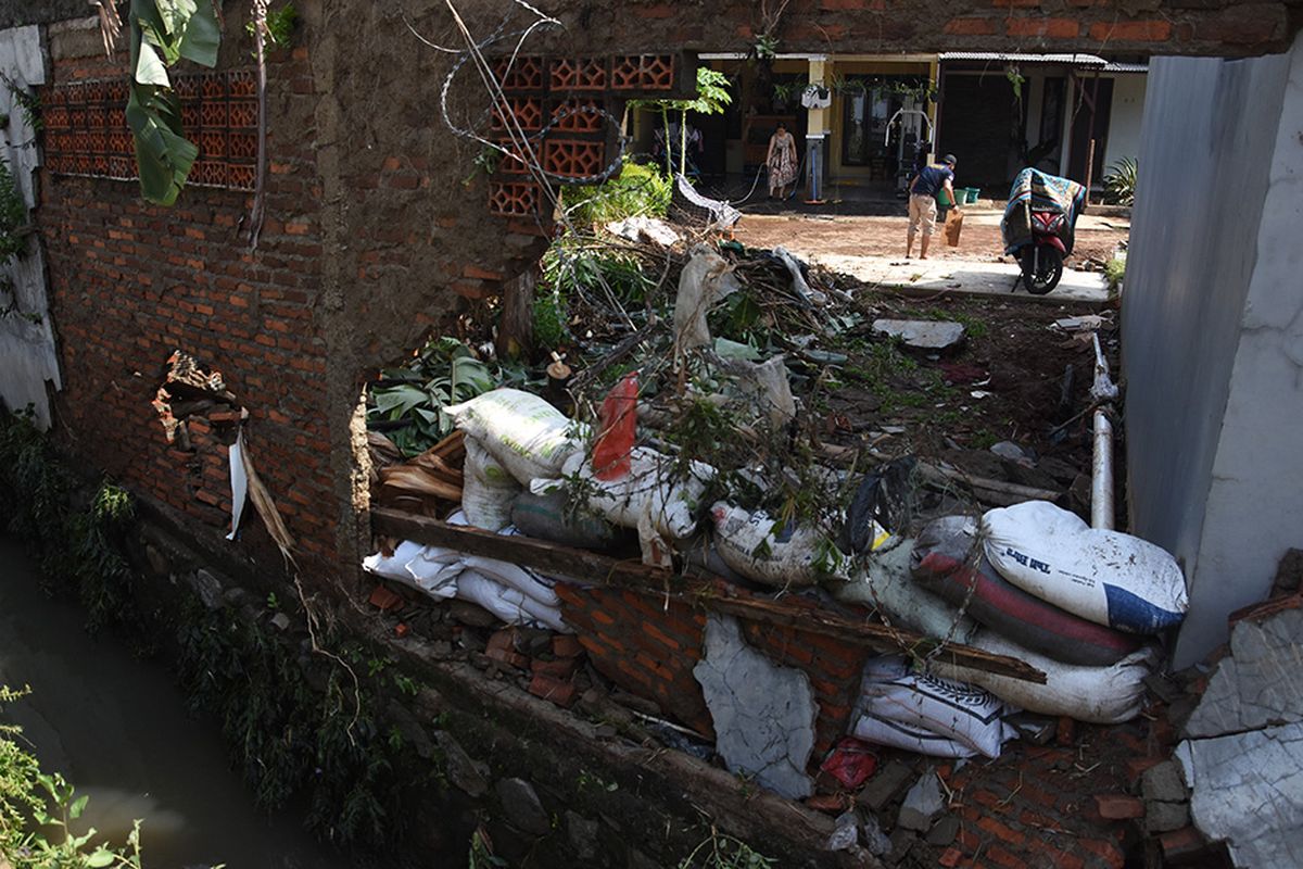 Warga membersihkan rumahnya pascabanjir yang merobohkan tembok pembatas kali di perumahan Green Malaka Residence, Ciracas, Jakarta, Minggu (11/10/2020). Banjir yang merendam sejumlah permukiman di Ciracas itu disebabkan karena meluapnya Kali Cipinang akibat hujan lebat pada Sabtu (10/10) kemarin