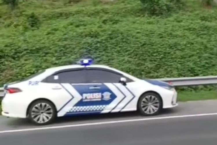 Mobil polisi parkir di bahu jalan tol saat mengevakuasi kasur terhempas dari atap mobil MPV.