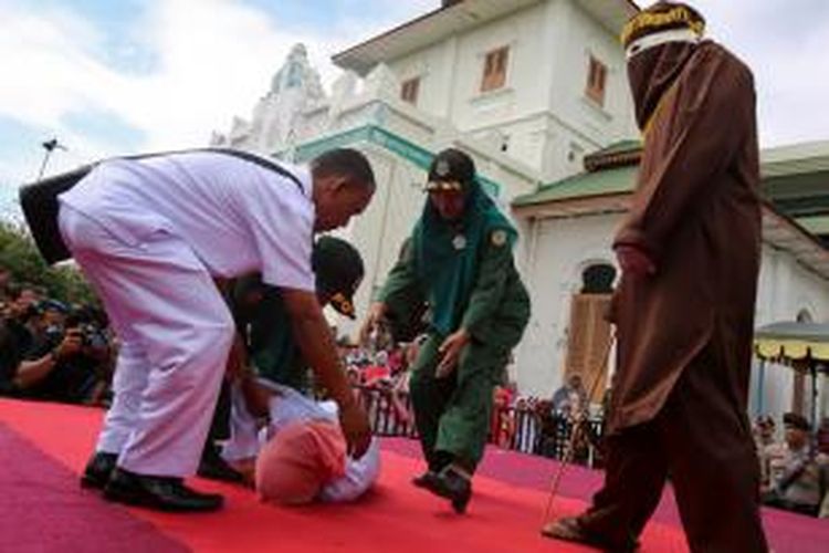 Petugas mengangkat terpidana pelanggar hukum syariat yang pingsan saat menjalani eksekusi hukuman cambuk di halaman Masjid Baiturrahim Ulee Lheue, Banda Aceh, Senin (28/12/2015).