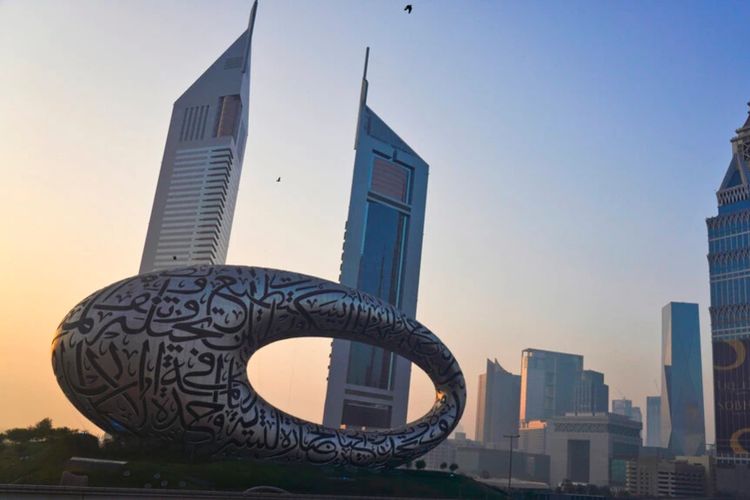 Pengendara sepeda berkendara di jalan raya utama dengan Museum of the Future dan Emirates Towers di belakang mereka di Dubai, Uni Emirat Arab.