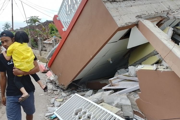 A man carrying a child walking in front of collapsed houses due to a 5.6-magnitude earthquake that struck the city of Cianjur in West Java on Wednesday, November 23, 2022.  
