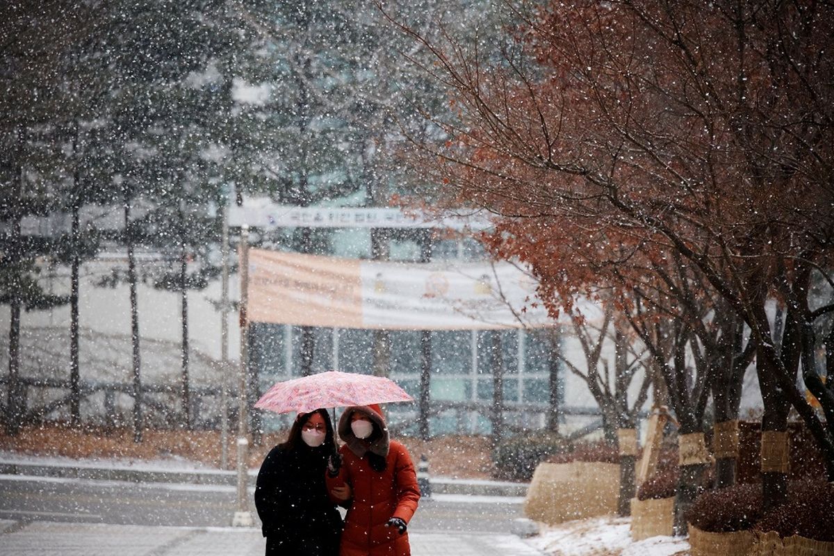 Wanita yang memakai masker sebagai langkah mencegah tertular penyakit virus corona (Covid-19) berjalan di bawah payung saat turun salju di Seoul, Korea Selatan, Senin (18/1/2021). ANTARA FOTO/REUTERS/Kim Hong-Ji/RWA/sa.
