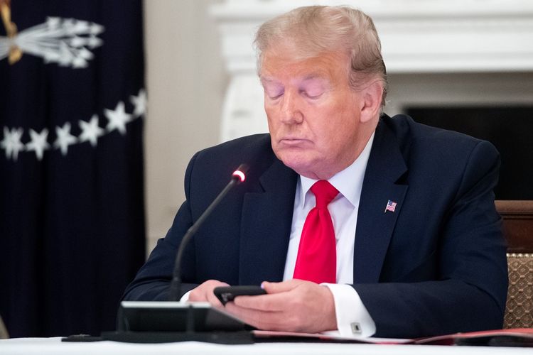 Presiden ke-45 Amerika Serikat Donald Trump memainkan smartphone dalam diskusi dengan para gubernur tentang pembukaan kembali ekonomi paska Covid-19 di Gedung Putih, Washington DC (18/6/2020).