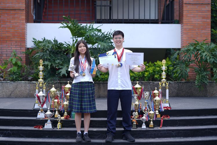 (ki-ka) Ava Mikayla Emmanoelle Kasih (14) dan Sean Levi Danuseputra (15) tengah berpose dengan memakai medali, dikelilingi piala, dan memegang sertifikat kompetisi mereka.