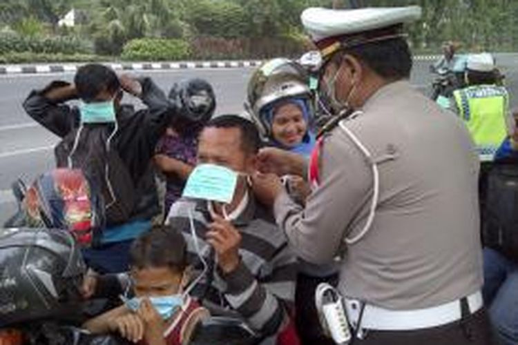 Polisi membagikan masker kepada pengendara sepeda motor di Kota Surabaya, Jumat (14/2/2014). Abu vulkanik akibat letusan Gunung Kelud juga mengguyur Kota Surabaya.