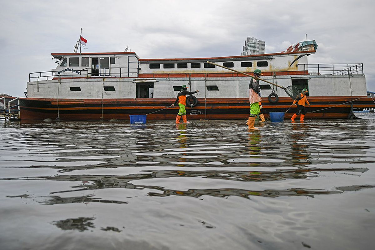 Petugas kebersihan beraktivitas saat banjir rob di Pelabuhan Kali Adem, Muara Angke, Jakarta, Jumat (1/1/2021). Banjir yang terjadi sejak Kamis (31/12/2020) itu dikarenakan pasang surut air laut.