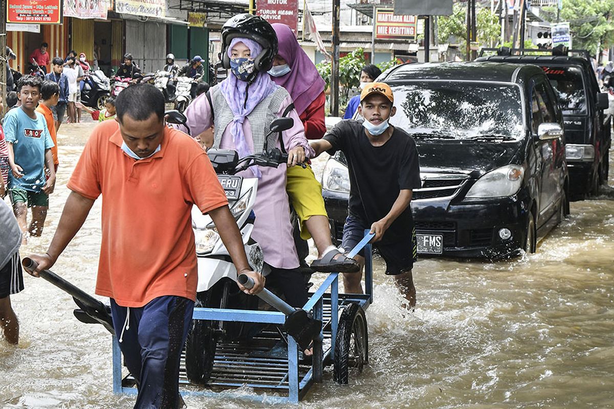 Dua orang pengendara motor menggunakan jasa gerobak untuk melintasi banjir di Jalan Bosih, Cibitung, Kabupaten Bekasi, Jawa Barat, Senin (8/2/2021). Menurut warga banjir menggenangi wilayah tersebut pada pukul 05.00 WIB akibat luapan aliran kali Jambe.