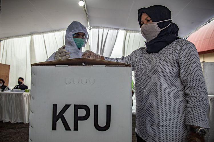 Petugas Kelompok Penyelenggara Pemungutan Suara (KPPS) berpakaian hazmat mendampingi warga memasukkan surat suara ke dalam kotak saat Simulasi Pemungutan dan Penghitungan Suara Pemilihan Bupati dan Wakil Bupati Semarang 2020 di Bergas, Kabupaten Semarang, Jawa Tengah, Minggu (29/11/2020). Simulasi tersebut untuk  memberikan pengetahuan terkait mekanisme dan prosedur proses pemungutan dan perhitungan suara Pilkada Kabupaten Semarang yang menerapkan protokol kesehatan di tengah pandemi COVID-19. ANTARA FOTO/Aji Styawan/aww.