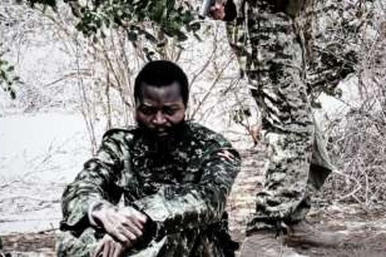 Seorang serdadu Uganda duduk dengan tangan terborgol, sebelum ditembak mati oleh orang yang berdiri di belakannya.  