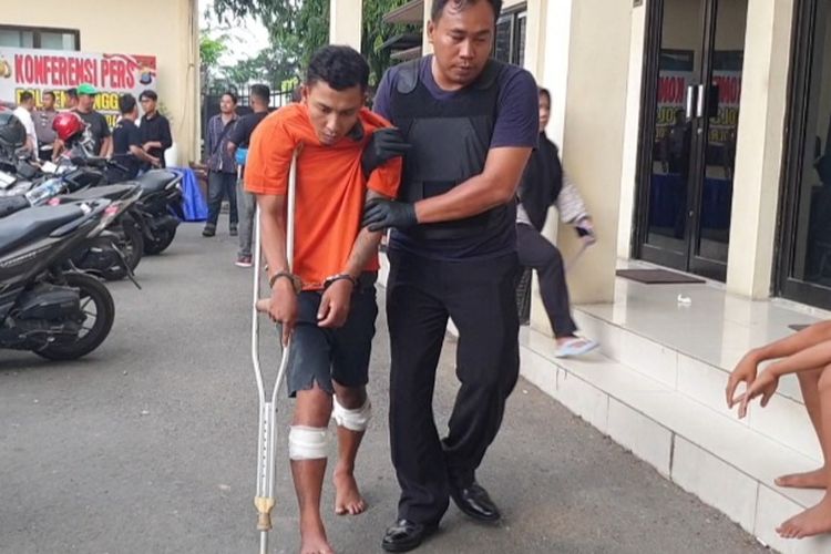 Raut wajah Iqbal Jauhari (26) tampak menahan rasa sakit akibat luka tembak di kedua kakinya saat melangkah untuk mengikuti konferensi pers di Polsek Sunggal pada Senin, 24 Juni 2024. 