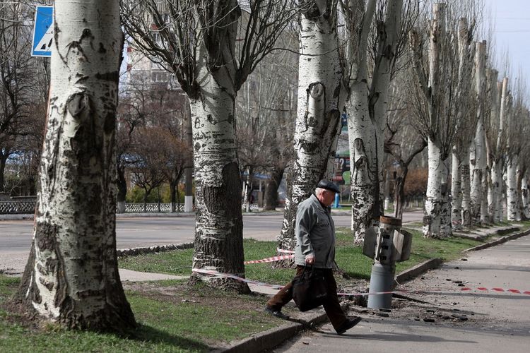 Seorang pria berjalan melewati ekor roket 300 mm yang tak meledak, tampaknya berisi bom kluster atau bom tandan yang diluncurkan dari peluncur roket ganda BM-30 Smerch di Lysychansk, wilayah Luhansk, 11 April 2022.