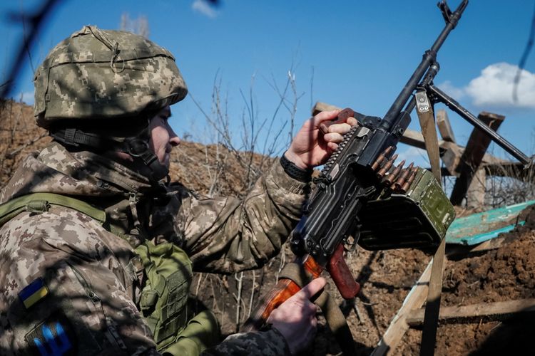Seorang praujurit membawa senapan mesin di parit dalam keadaan siaga di garis depan dekat desa Travneve, wilayah Donetsk, Ukraina, Senin (21/2/2022).
