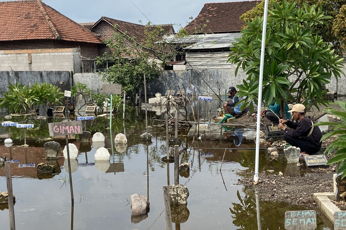 Warga yang memancing di tengah kuburan banjir di Desa Kalipecabean Sidoarjo, Selasa (17/12/2024).