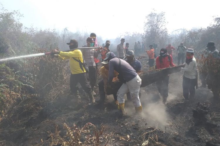 Tim Satgas Karhutla dan warga mengangkat kayu untuk dijadikan jembatan untuk melakukan pemadaman api yang membakar perkebunan karet masyarakat di Kelurahan Terkul, Kecamatan Rupat, Kabupaten Bengkalis, Riau, Jumat (22/2/2019).