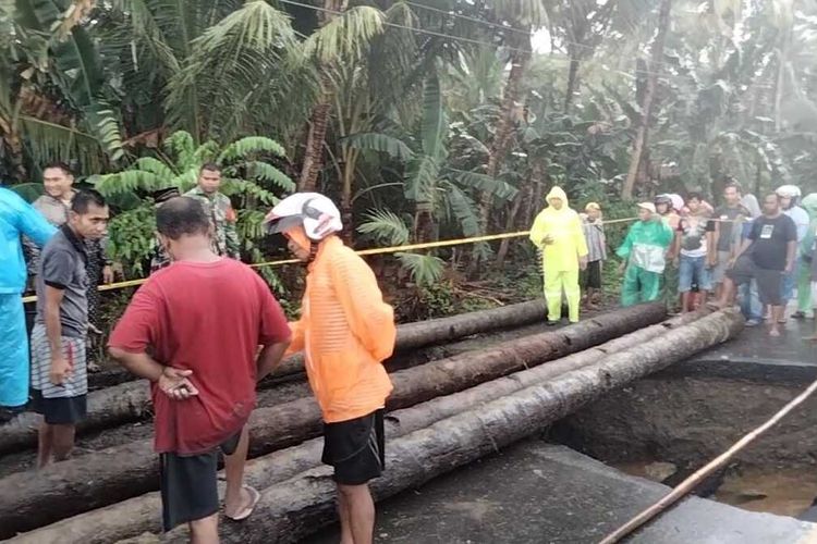 Warga bersama aparat kepolisian dan TNI bergotong royong membangun jembatan darurat dari batang pohon di jalan amblas di Dusun Aira, Kecamatan Amahai, Kabupaten Maluku Tengah, Minggu (17/7/2022)