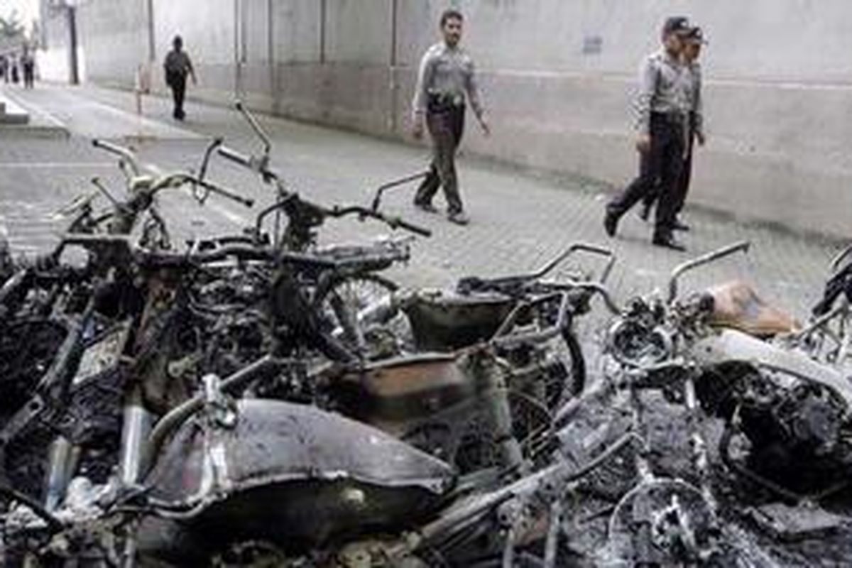 Sejumlah anggota kepolisian berjalan melintasi tumpukan bangkai sepeda motor yang dibakar massa pada kerusuhan di Temanggung, Selasa (9/2/2011).