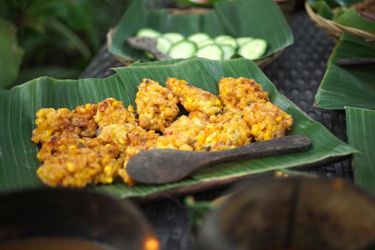 Ilustrasi dadar jagung yang disajikan di atas piring beralaskan daun pisang. 