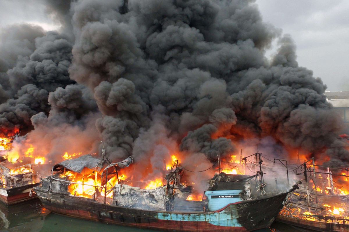 Asap tebal mengepul dari kapal-kapal yang terbakar di Pelabuhan Muara Baru, Jakarta Utara, Sabtu (23/2/2019). Hingga pukul 18.30 api masih terlihat membakar beberapa kapal, meski begitu proses pemadaman masih di lakukan,  di tengah angin yang kencang. (Warta Kota/Alex Suban)