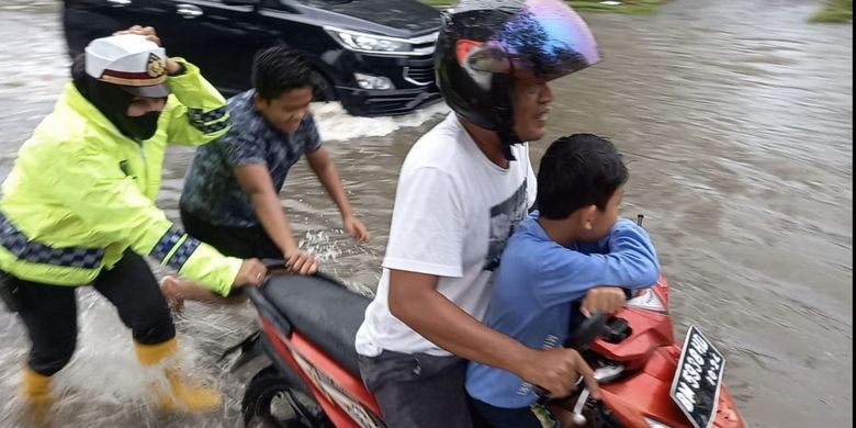 Seorang Polwan AKP Akira, dorong motor warga yang mogok akibat banjir di Jalan Sultan Syarif Kasim Kota Dumai, Riau. Rabu (27/10/2021).