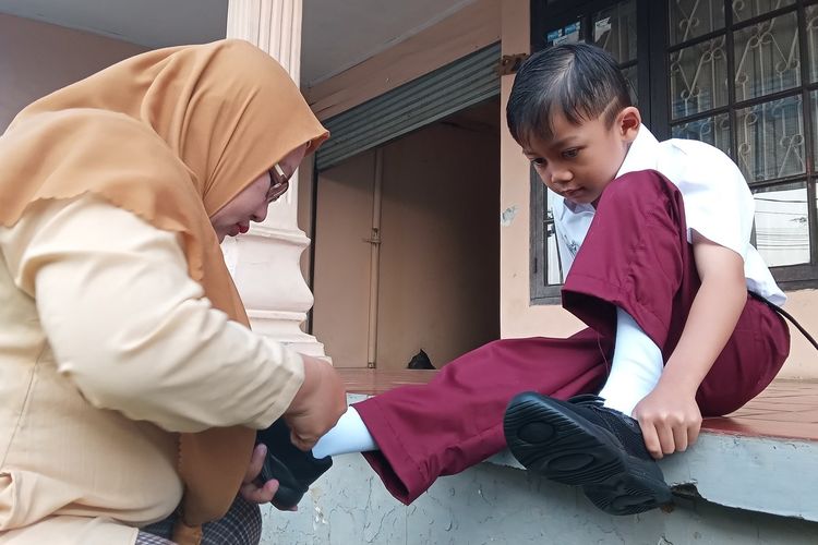 Fanny Ampiyani (42), ibu dua anak asal Kabupaten Cianjur, Jawa Barat ini tengah mengenakan sepatu anaknya yang bersiap ke sekolah di hari pertama tahun ajaran baru, Senin (17/7/2023).