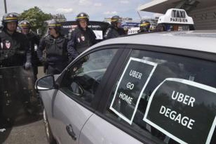 Polisi antihuru-hara berdiri di samping taksi yang ditempel poster yang berbunyi 'Uber pulang' dan 'Uber keluar' dalam demonstrasi di Paris, 25 Juni 2015. Sopir taksi di Paris melakukan aksi mogok dengan menutup jalan Bandara Charles de Gaulle.