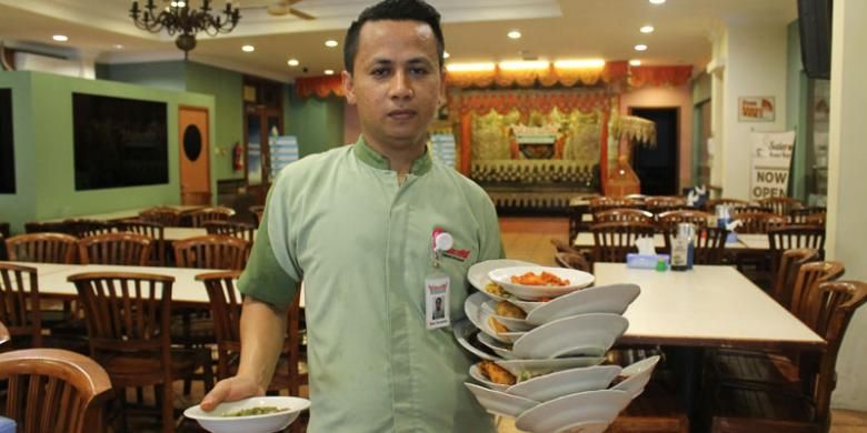 Suasana khas Restoran Padang, pelayannya membawa setumpuk piring di tangan.