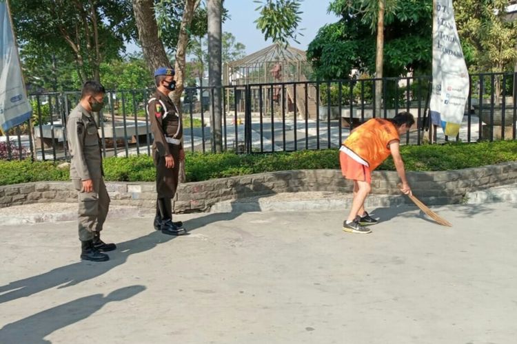 Seorang warga Cianjur, Jawa Barat sedang menjalani kerja sosial di kawasan alun-alun, Senin (27/7/2020) setelah terjaring razia tidak memakai masker.