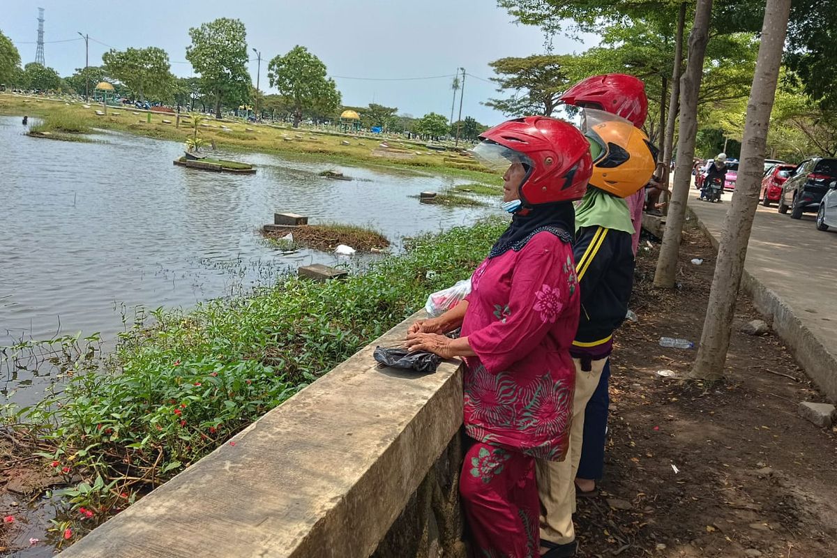 Anto (36), bersama dengan Ibu dan Istrinya saat berziarah ke makam mertuanya yang tergenang banjir di TPU Semper, Cilincing, Jakarta Utara, 