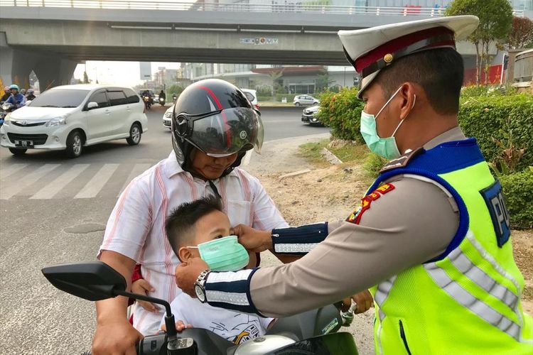 Salah satu petugas Satlantas Polresta Pekanbaru memasangkan memasangkan masker kepada seprang anak yang mengendarai sepeda bersama orang tuanya di Jalan Jenderal Sudirman, Pekanbaru, Riau, Jumat (9/8/2019).