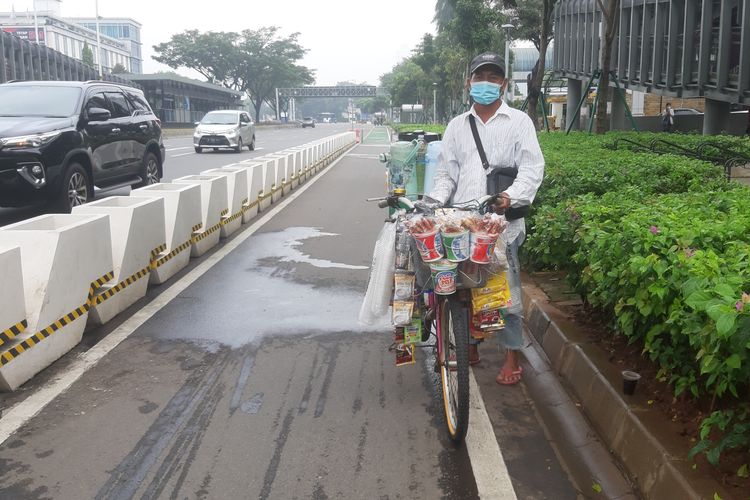 Zaini, salah seorang penjual kopi keliling saat melintas di jalur sepeda terproteksi di Jalan Sudirman, Jakarta, Sabtu (29/5/2021).