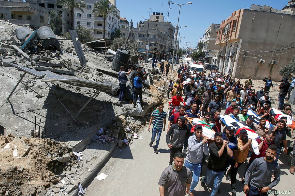 Mourners carry the bodies of Palestinians who were killed amid a flare-up of Israeli-Palestinian violence during their funeral near the remains of a building destroyed in Israeli airstrikes at the Beach refugee camp in Gaza City (15/5/2021)