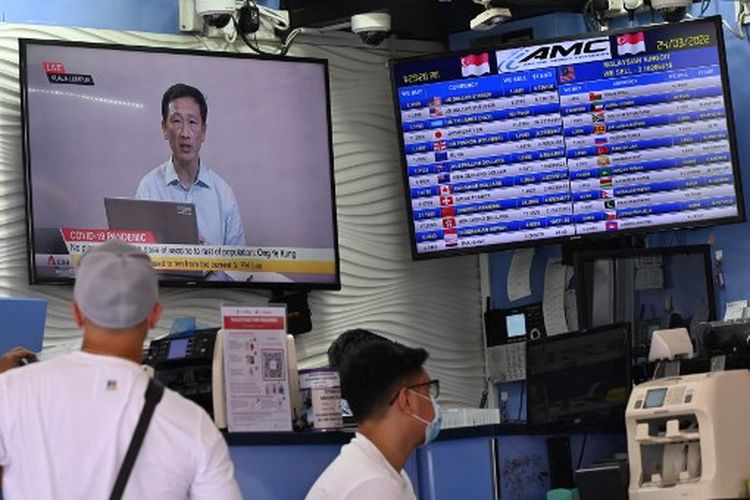 Orang-orang berjalan melewati layar di tempat penukaran uang yang menunjukkan Menteri Kesehatan Singapura Ong Ye Kung berbicara langsung di televisi nasional tentang pelonggaran pembatasan Covid-19 di Singapura pada 24 Maret 2022. 
