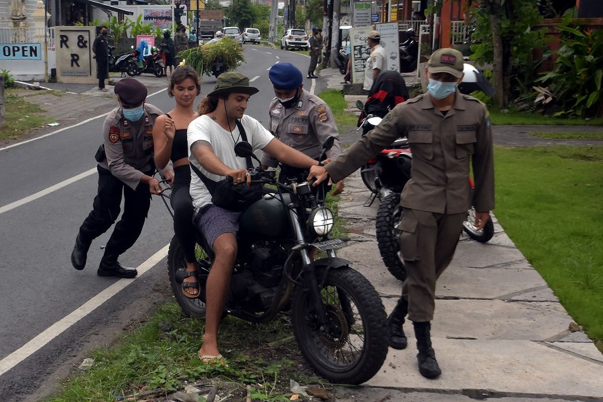 Anggota Polisi dan Satpol PP Kabupaten Badung menghentikan warga negara asing (WNA) yang melanggar protokol kesehatan saat operasi penertiban prokes dalam Pemberlakuan Pembatasan Kegiatan Masyarakat (PPKM) skala mikro di Desa Canggu, Badung, Bali, Jumat (25/6/2021). Tim satgas gabungan menindak sebanyak 18 orang WNA yang berasal dari berbagai negara tersebut untuk memberikan efek jera agar menerapkan protokol kesehatan dalam upaya pencegahan penyebaran varian baru COVID-19 di kawasan pariwisata itu. ANTARA FOTO/Nyoman Hendra Wibowo/aww.
