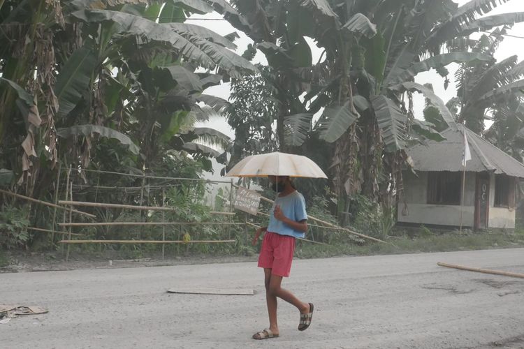 Seorang anak kecil menggunakan payung untuk melindungi diri dari abu vulkanis Gunung Lewotobi Laki-laki di Flores Timur, NTT, Selasa (2/1/2024). (Kompas.com/ Serafinus Sandi)
