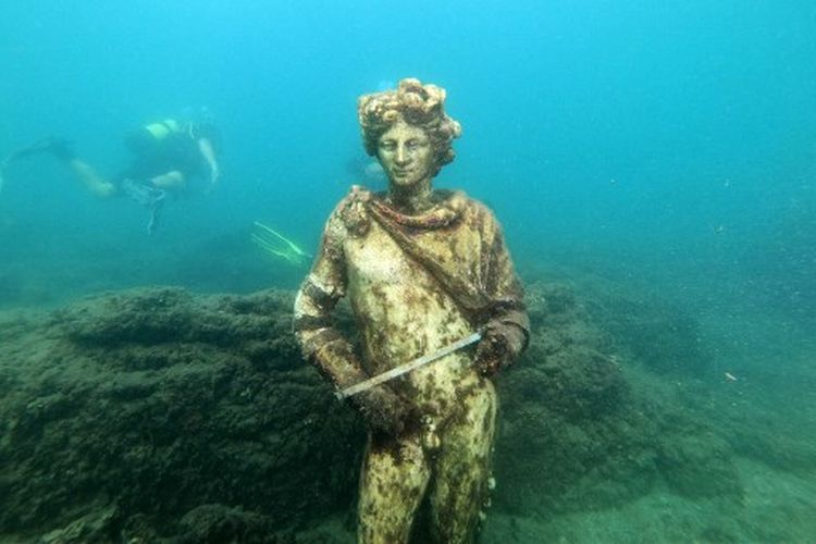 Dalam foto yang diambil pada 18 Agustus 2021, pemandu selam menunjukkan kepada wisatawan salinan patung asli yang disimpan di Museum Baiae, mewakili Dionysus dengan mahkota ivy di Nymphaeum of punta Epitaffio, kota Romawi kuno Baiae yang terendam di Baiae Underwater Park, bagian dari situs kompleks Taman Arkeologi Campi Flegrei di Pozzuoli dekat Napoli.