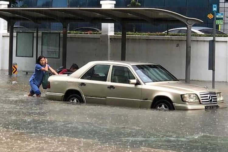 Seorang perempuan terpaksa mendorong mobilnya yang terendam banjir di kawasan Bedok Utara, Singapura, Senin (8/1/2017).