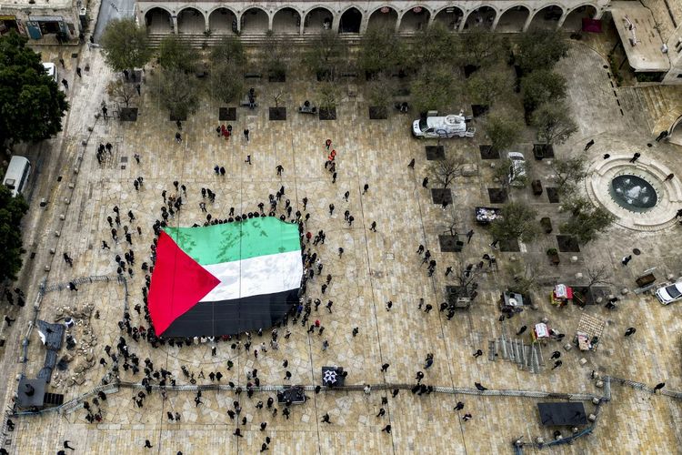 Foto udara ini menunjukkan para pengunjung yang membentangkan bendera Palestina raksasa saat mereka berkumpul di Alun-Alun Palungan di luar Gereja Kelahiran di kota alkitabiah Bethlehem di Tepi Barat yang diduduki pada Malam Natal (menurut tradisi Barat) pada 24 Desember 2023.