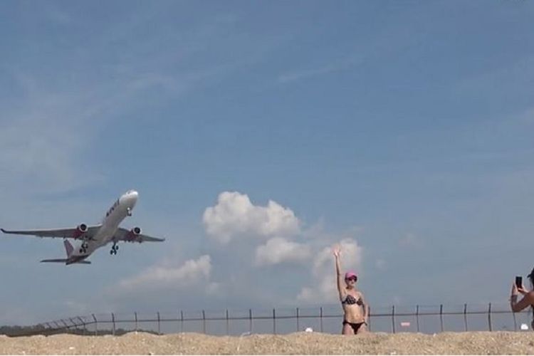 Banyak turis yang berada di pantai tak jauh dari bandara internasional Phuket, Thailand menggunakan momen pesawat akan mendarat sebagai latar belakang foto mereka.