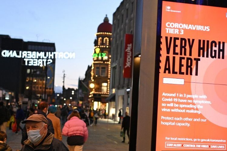 Seorang pejalan kaki mengenakan masker untuk melindungi diri dari Covid-19, di dekat papan informasi aturan Tier 3 di Inggris guna mengatasi wabah virus corona. Foto diambil di Newcastle-upon Tyne, Inggris, pada 19 Desember 2020.