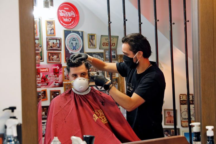 Seorang tukang potong rambut tengah memotong rambut pelanggan di kota Thessaloniki, Yunani, pada 4 Mei 2020. Yunani mulai memberlakukan pencabutan gradual lockdown untuk memerangi virus corona.