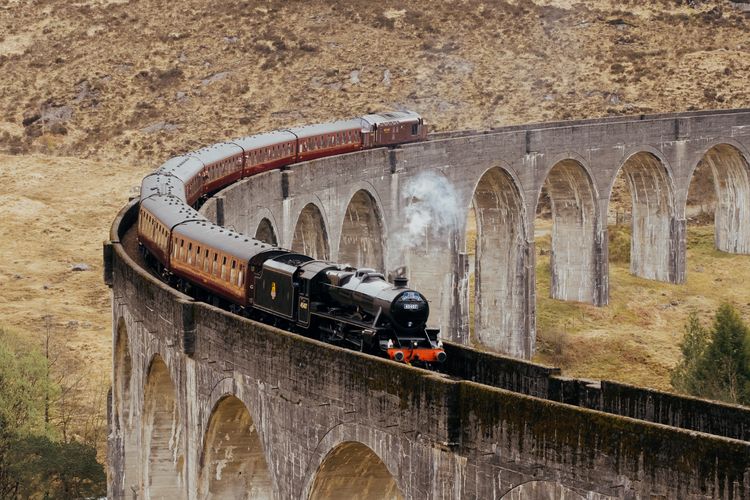 Ilustrasi Jacobite Steam Train (Kereta Uap Jacobite) yang mirip kereta Hogwarts Express di film Harry Potter saat melintasi Jembatan Glenfinnan.