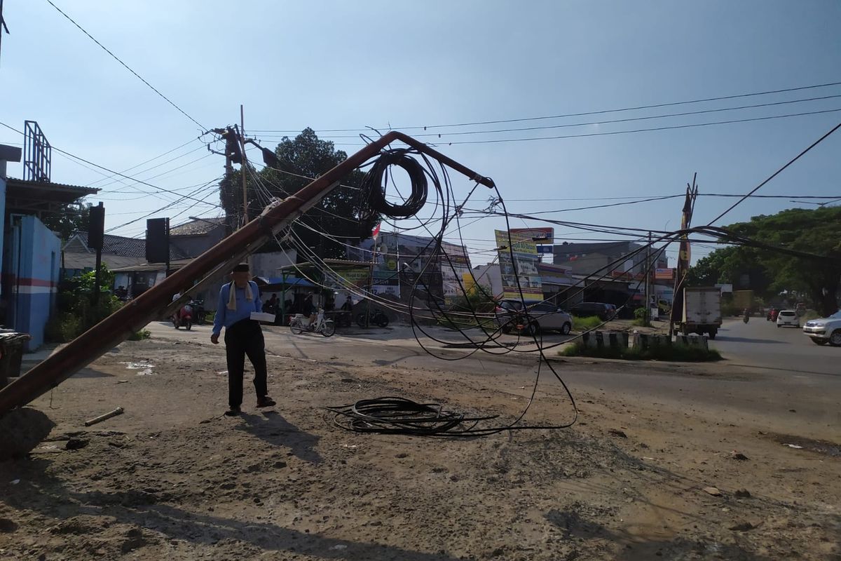 Seorang warga melintas di bawah tiang kabel telepon yang nyaris tumbang lantaran terseret kontainer di Jalan Ciater, Tangerang Selatan, Kamis (16/9/2021). 